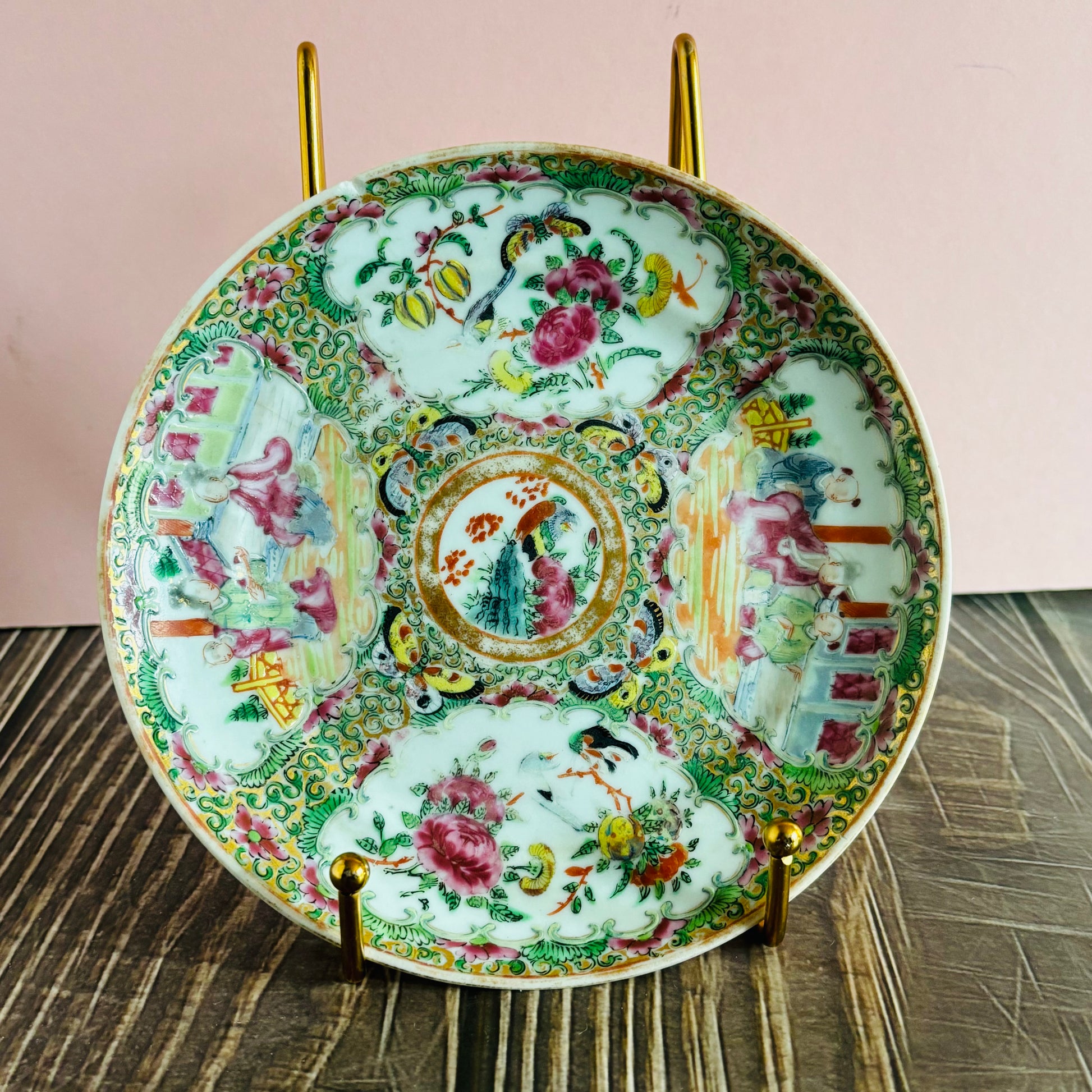 Decorative ceramic plate with intricate designs on a stand against a pink background