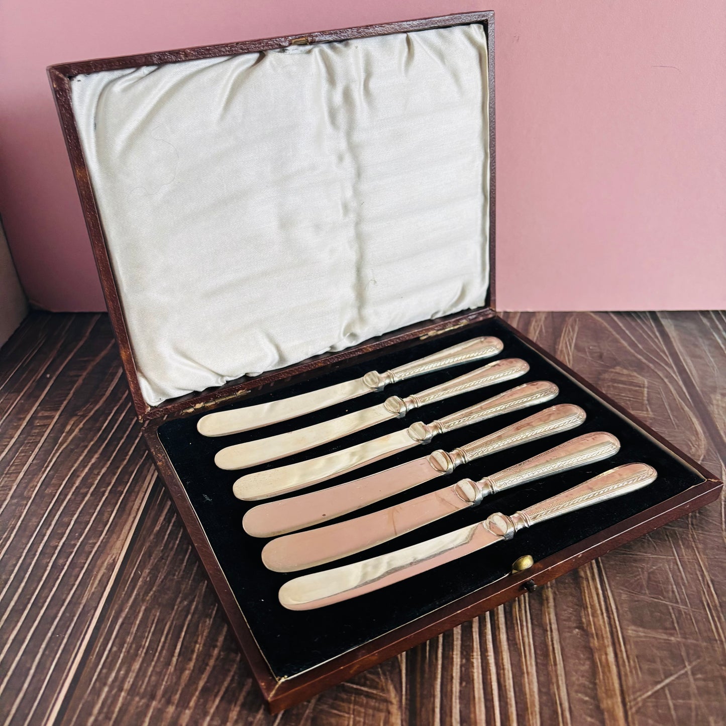 Set of vintage knives in a box on a wooden surface with a pink wall background