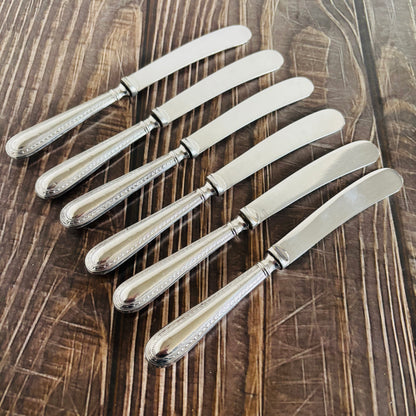Set of six silver butter knives on a wooden surface