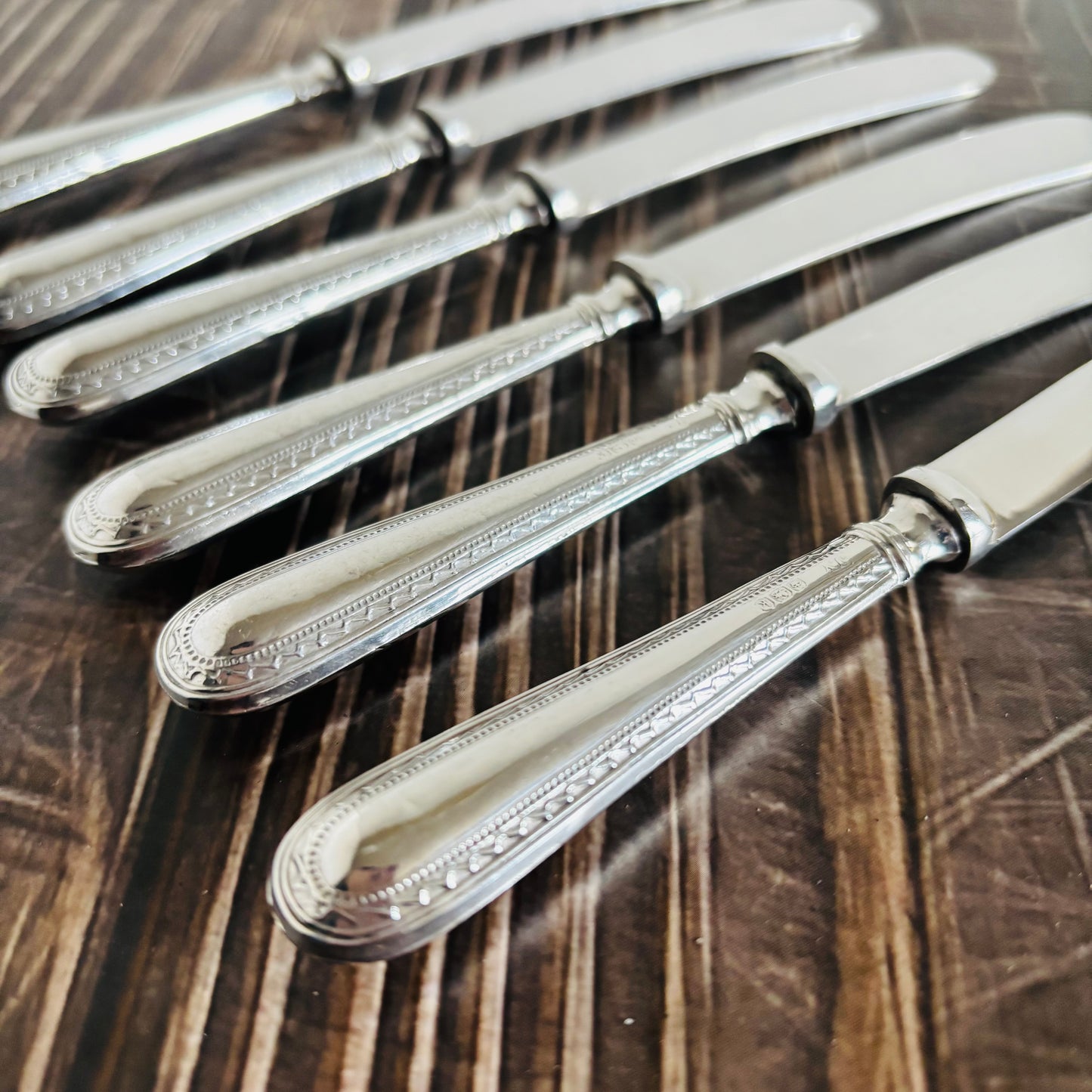 Set of silver knives with decorative handles on a wooden surface