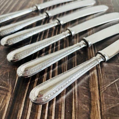 Set of silver knives with decorative handles on a wooden surface