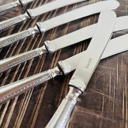 Set of silver butter knives with decorative handles on a wooden surface