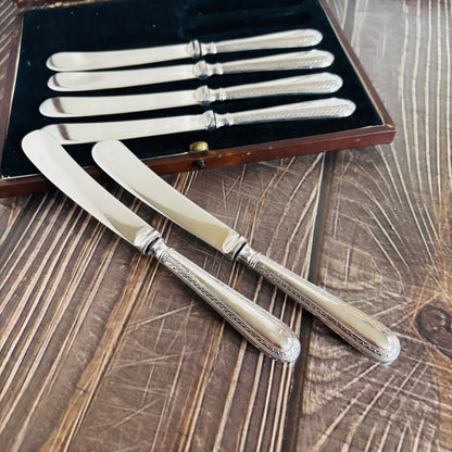 Set of silver knives with decorative handles on a wooden surface