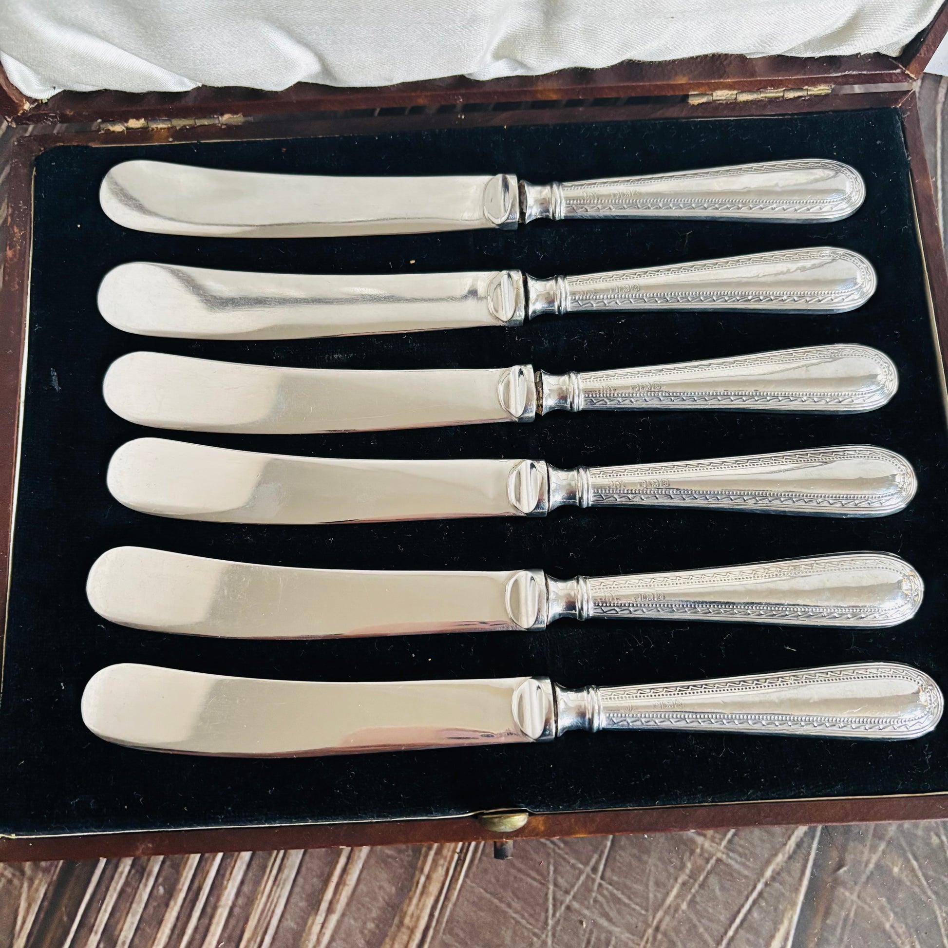 Set of six silver butter knives in a case on a wooden surface.