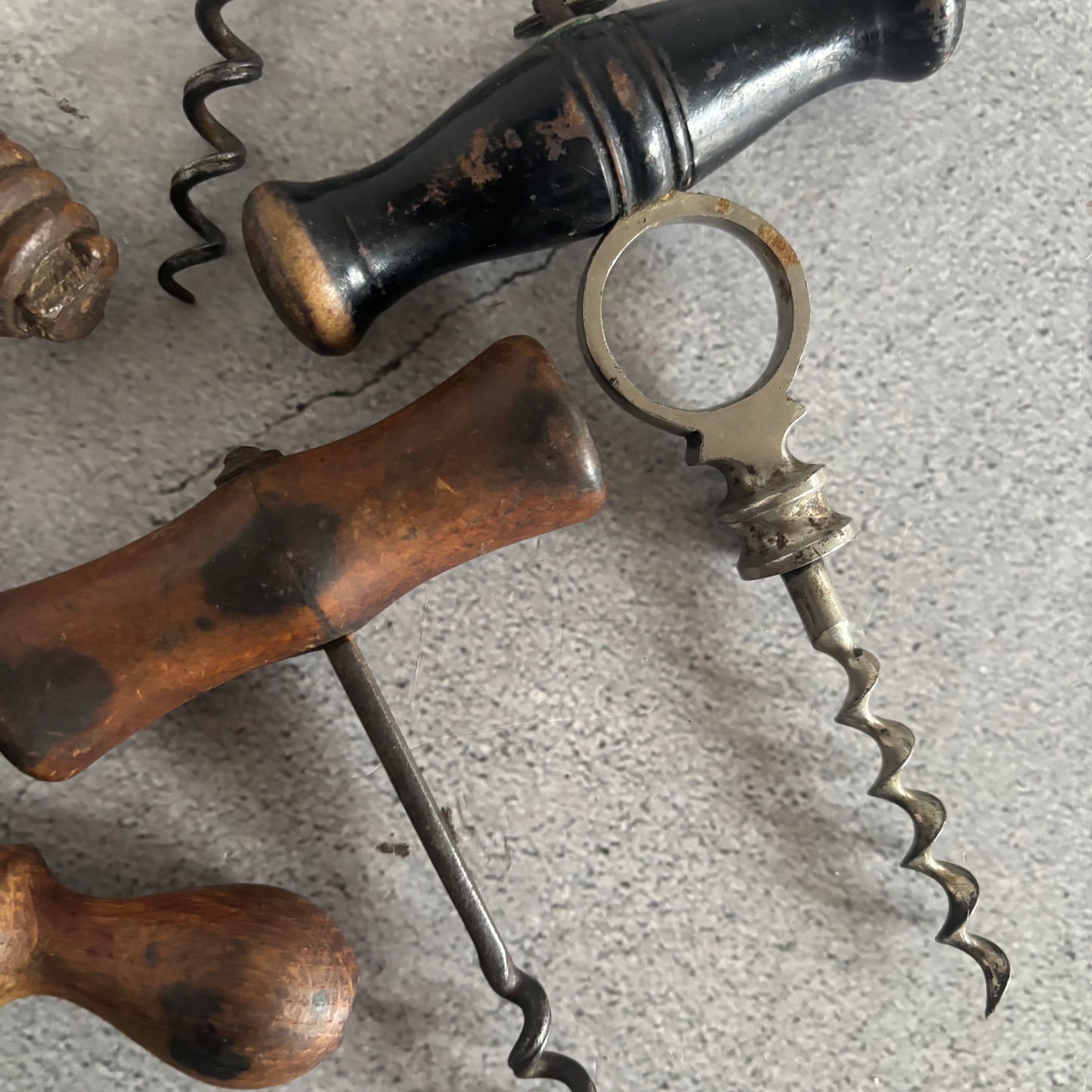 Close-up of antique corkscrews with wooden and metal handles on a textured surface.