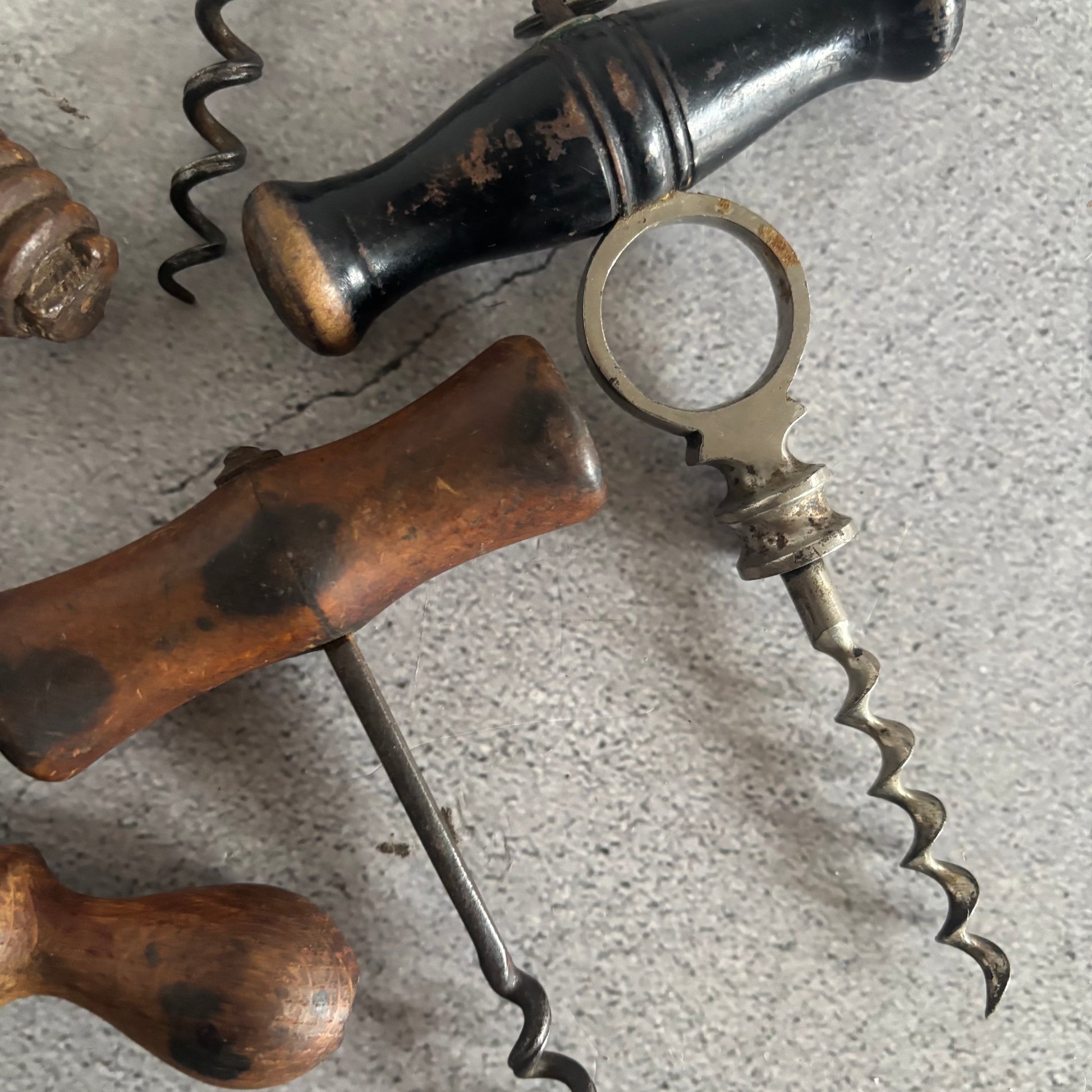 Close-up of antique corkscrews with wooden and metal handles on a textured surface.