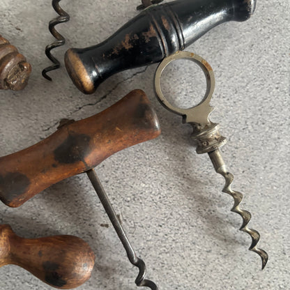 Close-up of antique corkscrews with wooden and metal handles on a textured surface.
