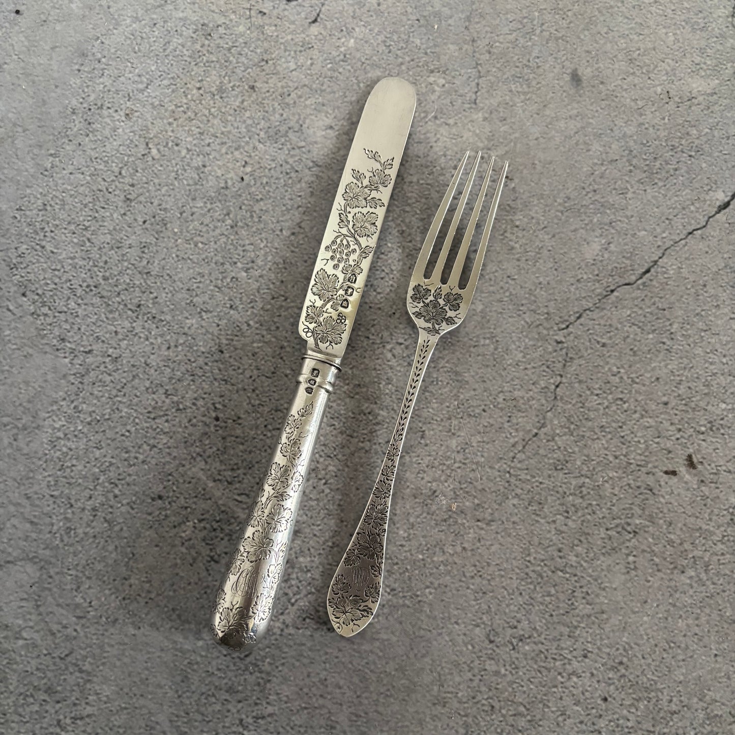 Antique Silver Fully Engraved Knife and Fork Duo on a textured grey surface