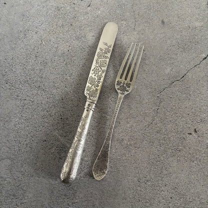 Antique Silver Fully Engraved Knife and Fork Duo on a textured grey surface