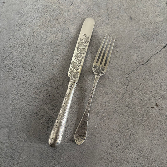 Antique Silver Fully Engraved Knife and Fork Duo on a textured grey surface