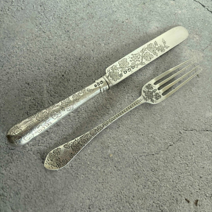 Decorative silver fork and knife set on a gray surface