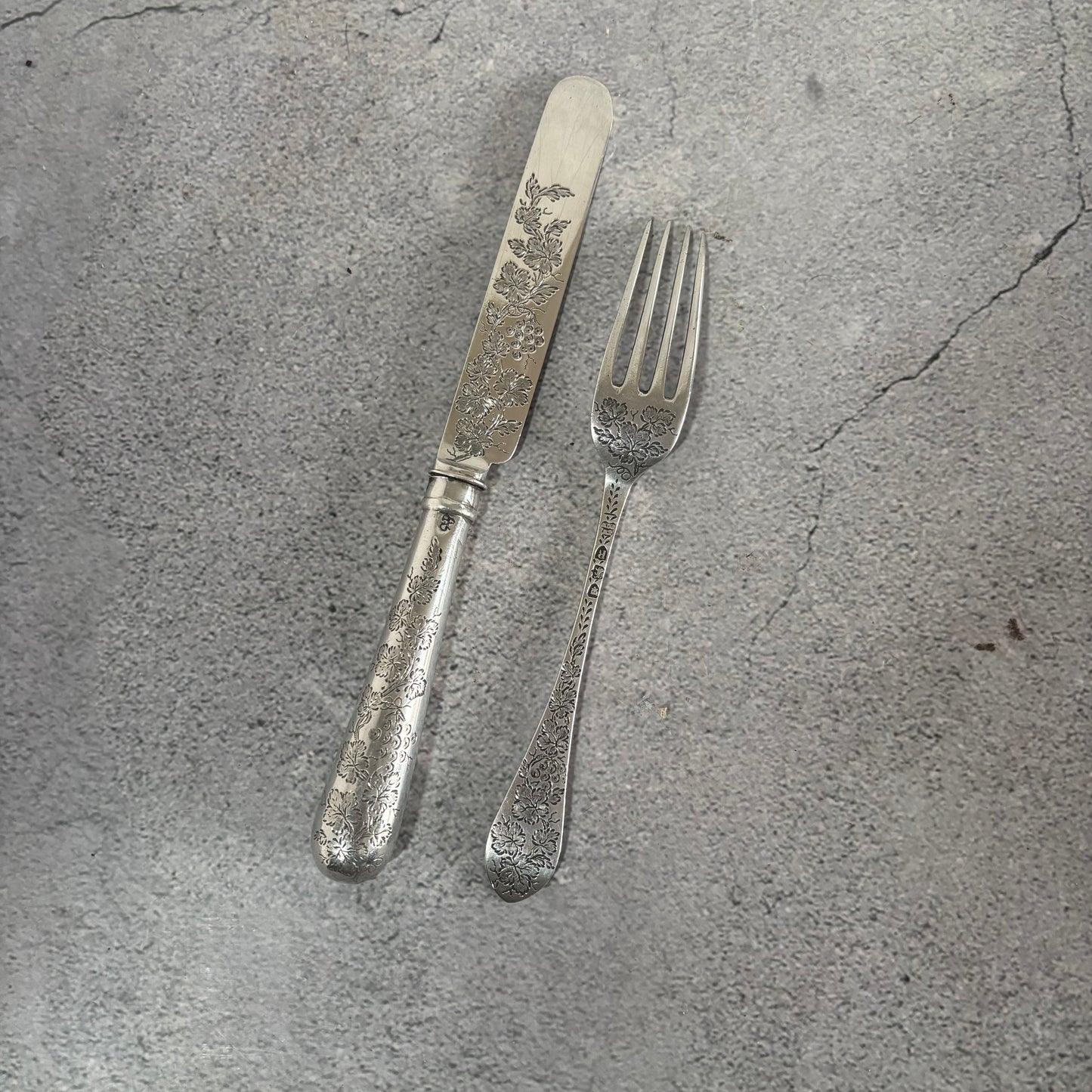 Antique Silver Fully Engraved Knife and Fork Duo on a textured gray surface
