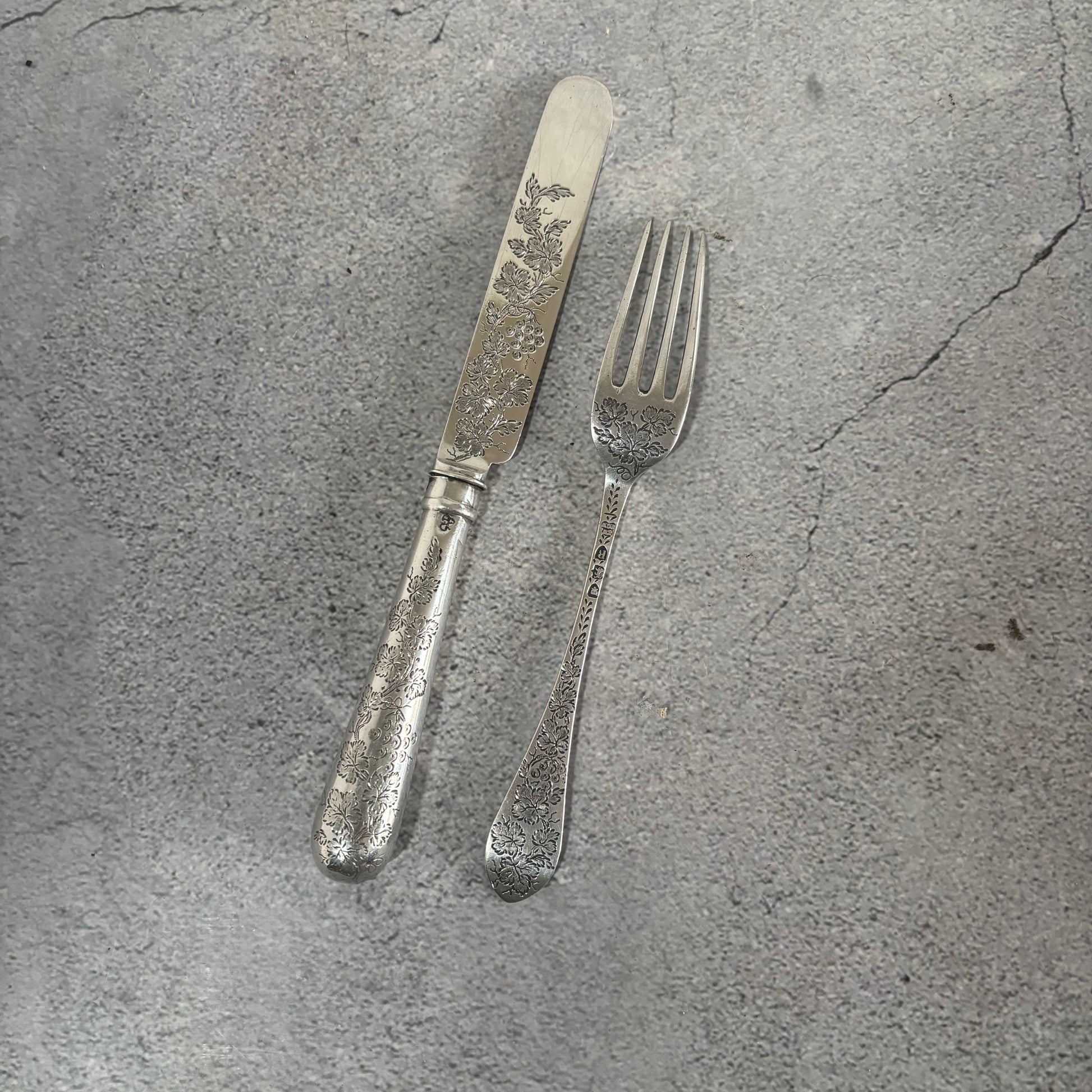 Antique Silver Fully Engraved Knife and Fork Duo on a textured gray surface