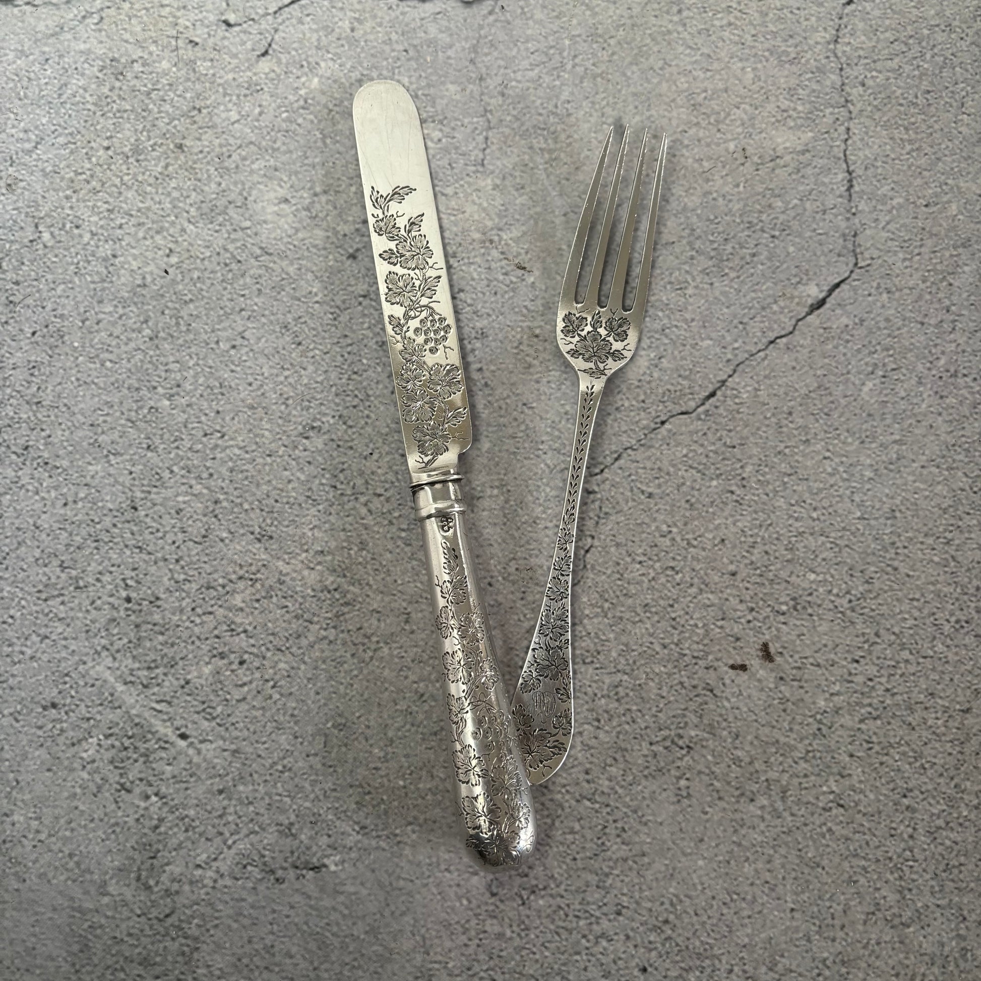 Silver knife and fork with floral patterns on a gray concrete surface