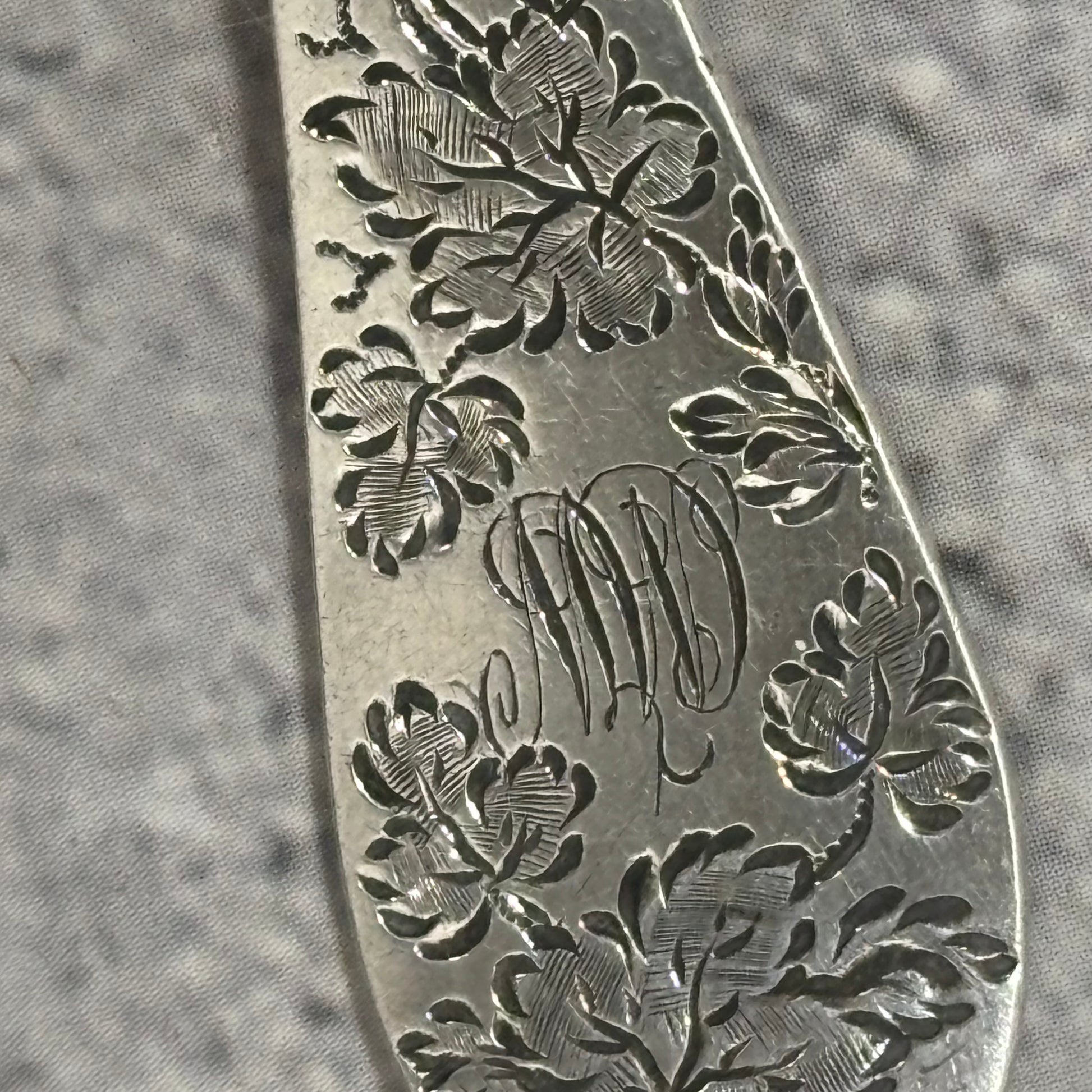 Close-up of a silver fork with floral engravings and initials on a textured gray background