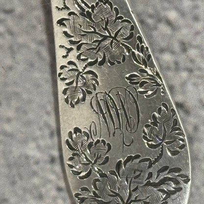 Close-up of a silver fork with floral engravings and initials on a textured gray background