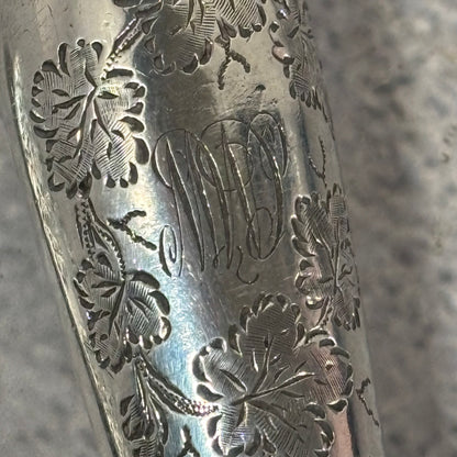 Close-up of an engraved silver knife with floral patterns and a MD signature.