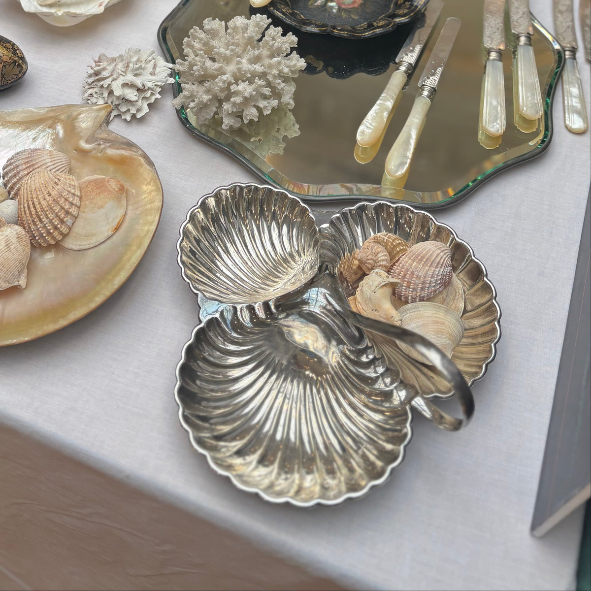 Table with decorative items including shell plates, coral, and silverware on a white tablecloth.