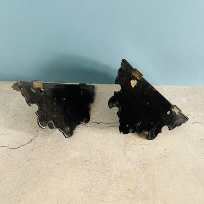 Two decorative metal brackets on a concrete surface with a light blue wall in the background.