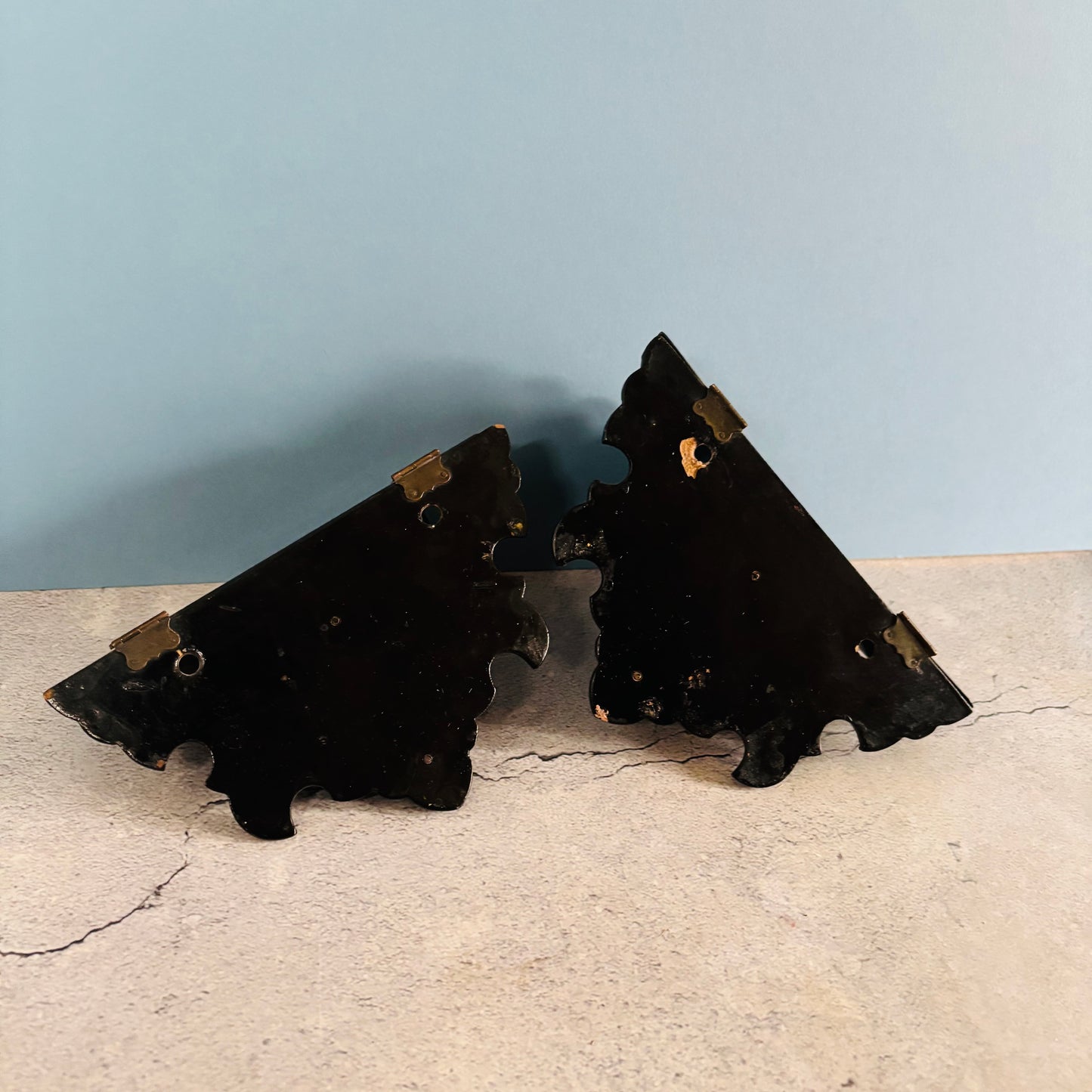 Two black decorative brackets on a beige surface with a light blue wall background.