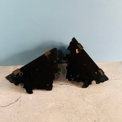 Two black decorative brackets on a beige surface with a light blue wall background.