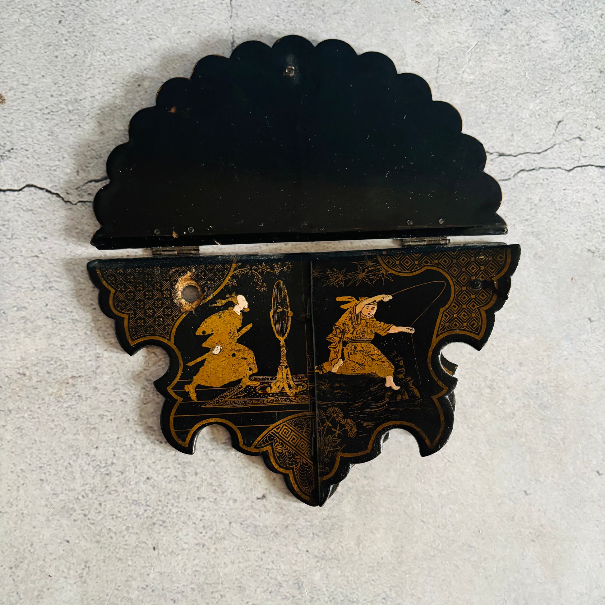 Decorative black and gold wall piece with figures on a textured gray background