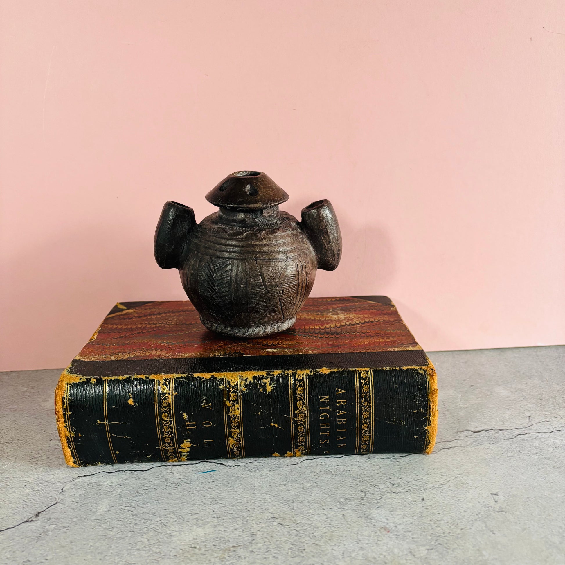 Antique African Clay Ink Pot From Kano Nigeria on an old book with a pink background