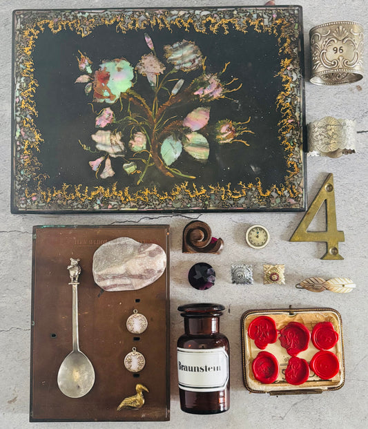 Collection of vintage items including a decorative box with floral design, a spoon, a bottle, and other small objects on a textured surface.
