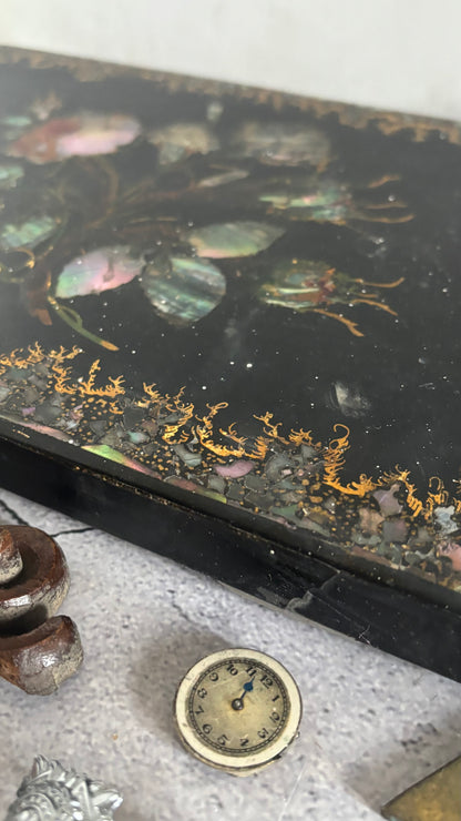 Decorative box lid with floral design and gold accents on a textured surface.