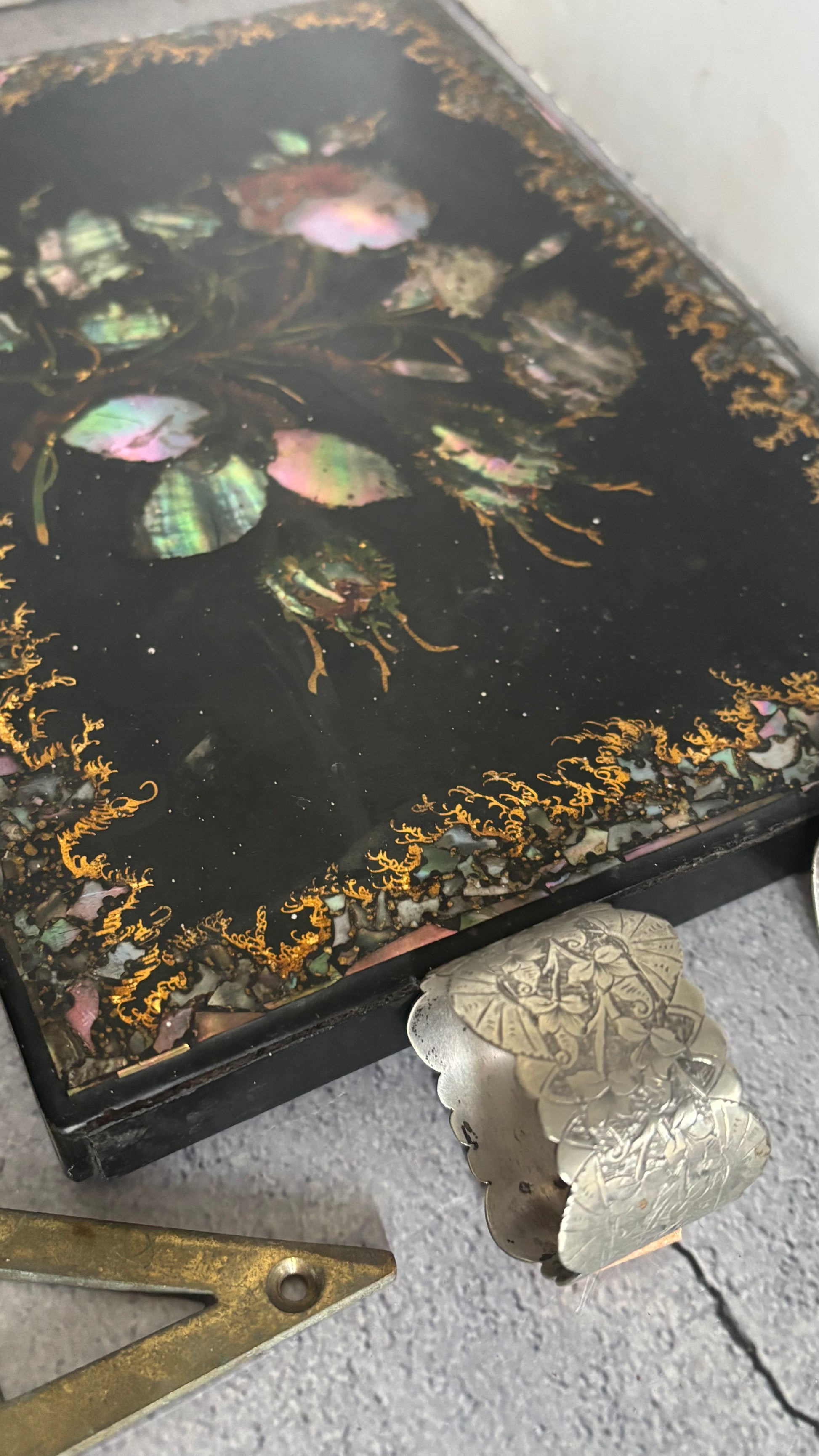 Decorative box lid with floral design and a silver napkin ring on a textured surface