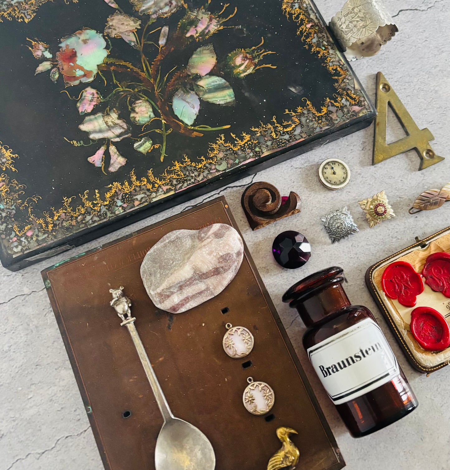 Vintage items including a decorative box, bottle labeled 'Braunstein', and small objects on a textured surface.