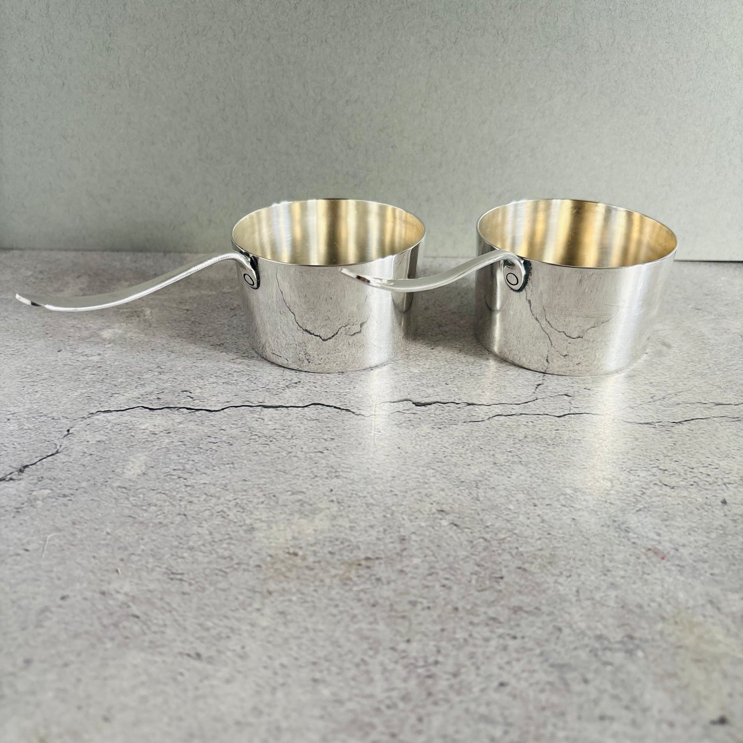 Pair of silver brandy pots on a concrete surface with a gray background