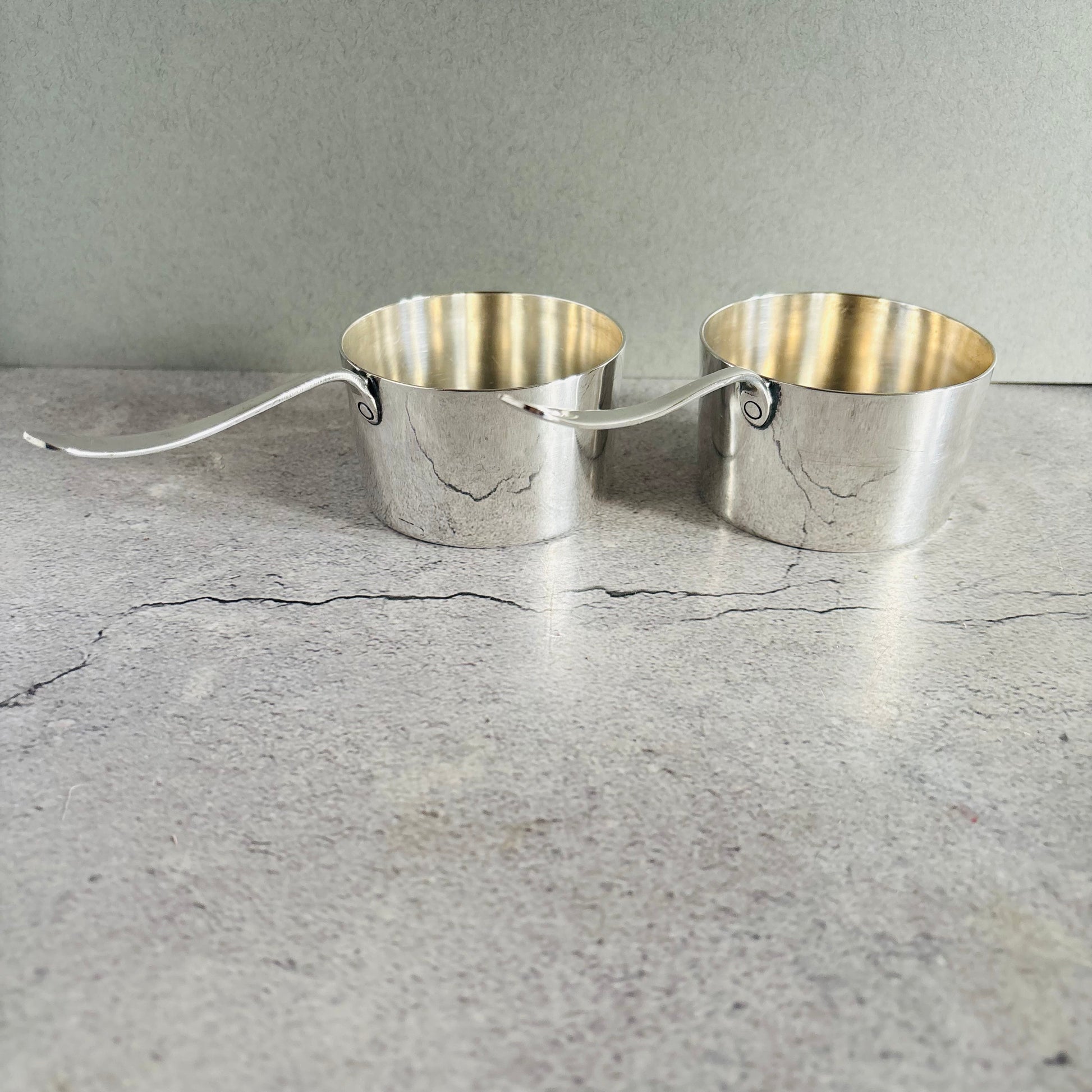 Pair of silver brandy pots on a concrete surface with a gray background