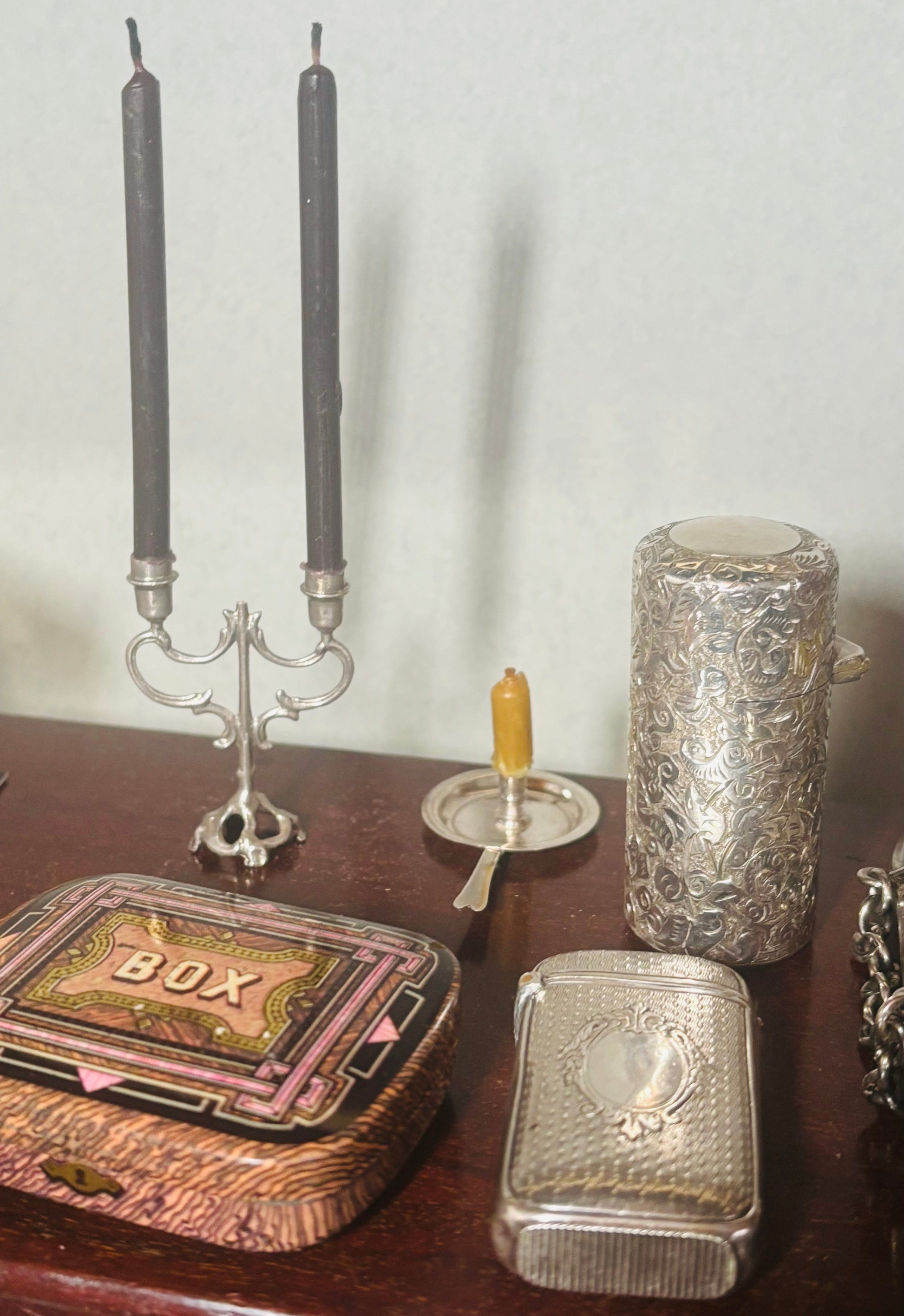 Decorative items including a silver box, candlesticks, and a textured container on a wooden surface.