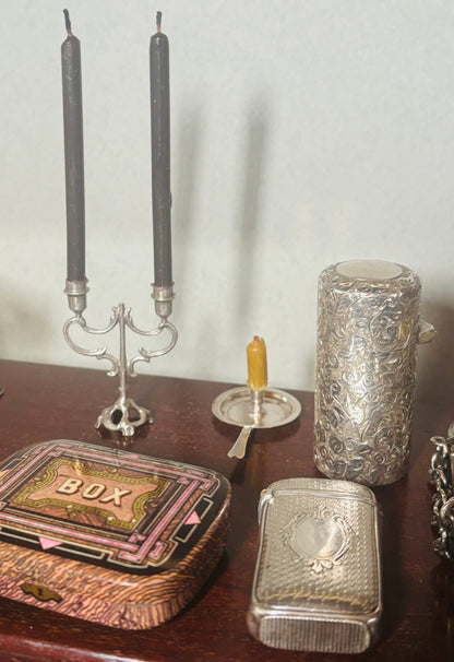 Decorative items including a silver box, candlesticks, and a textured container on a wooden surface.