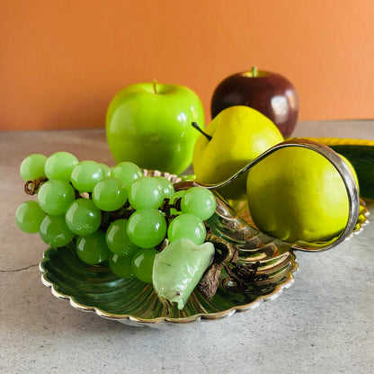 Fruit including grapes, apples, and a pear on a decorative silver platter with an orange wall background.