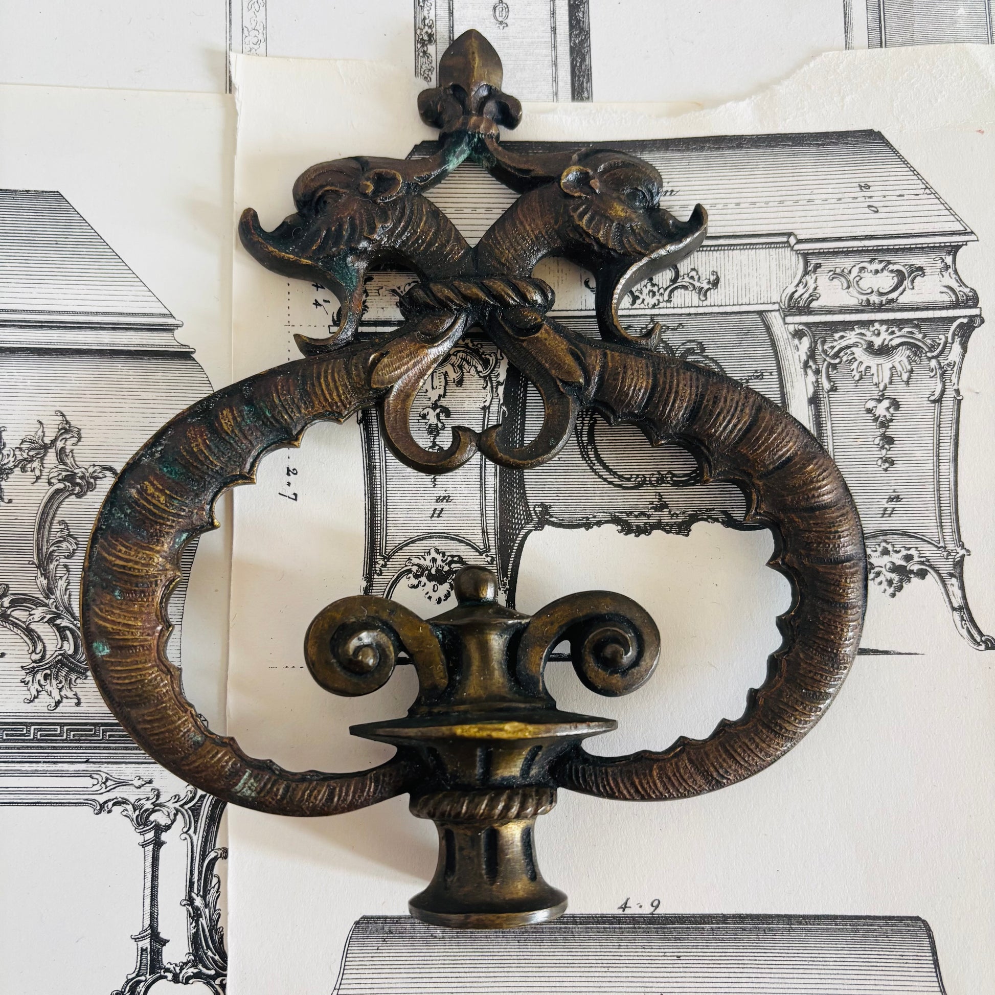 Decorative bronze wall piece with intricate design on a background of architectural drawings.