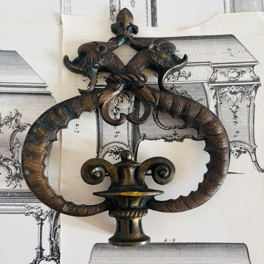 Decorative bronze wall piece with intricate design on a background of architectural drawings.