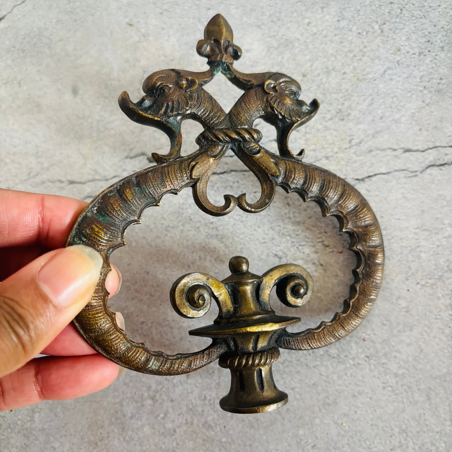 Decorative bronze finial held by a hand on a grey surface