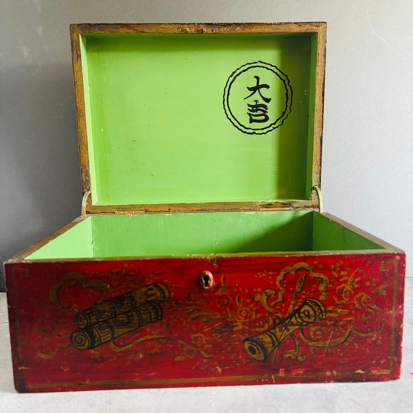 Open wooden box with green interior and red exterior featuring intricate designs and a logo.