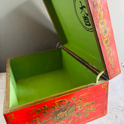 Open red and green wooden box with intricate designs on a gray background