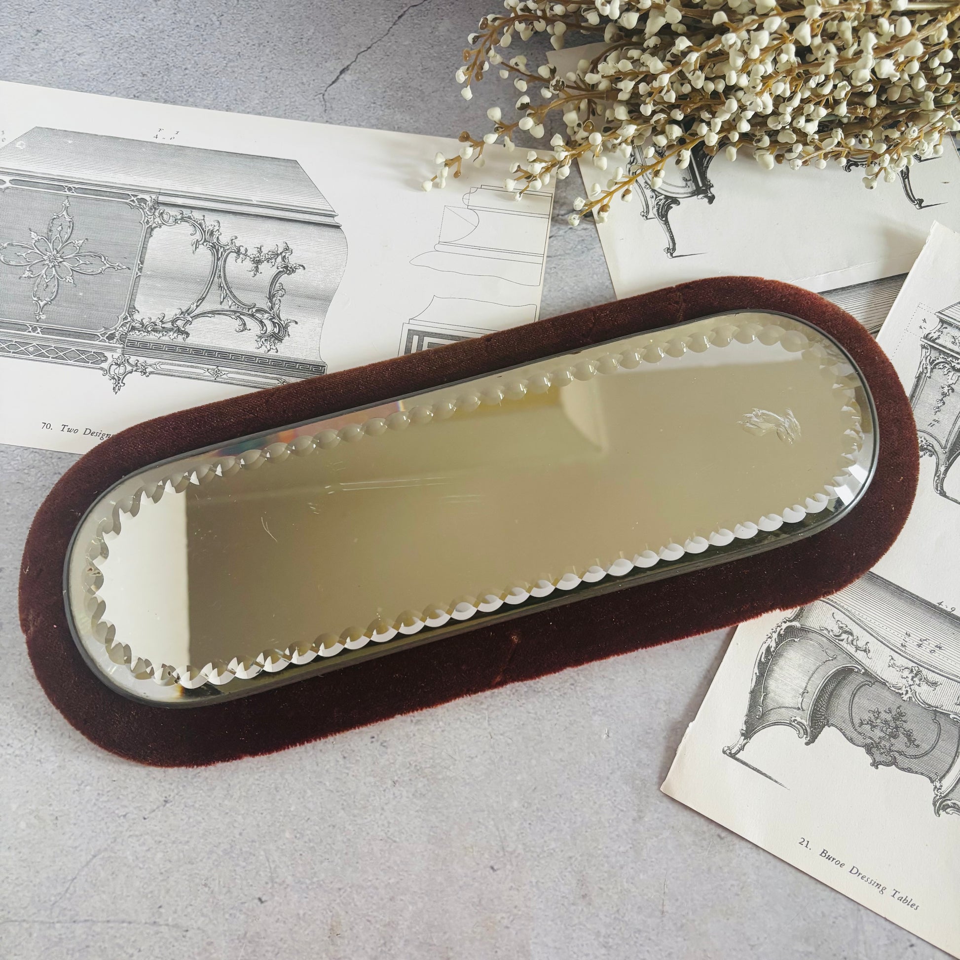 Rectangular mirror with velvet frame on a textured surface with dried flowers and vintage books plates
