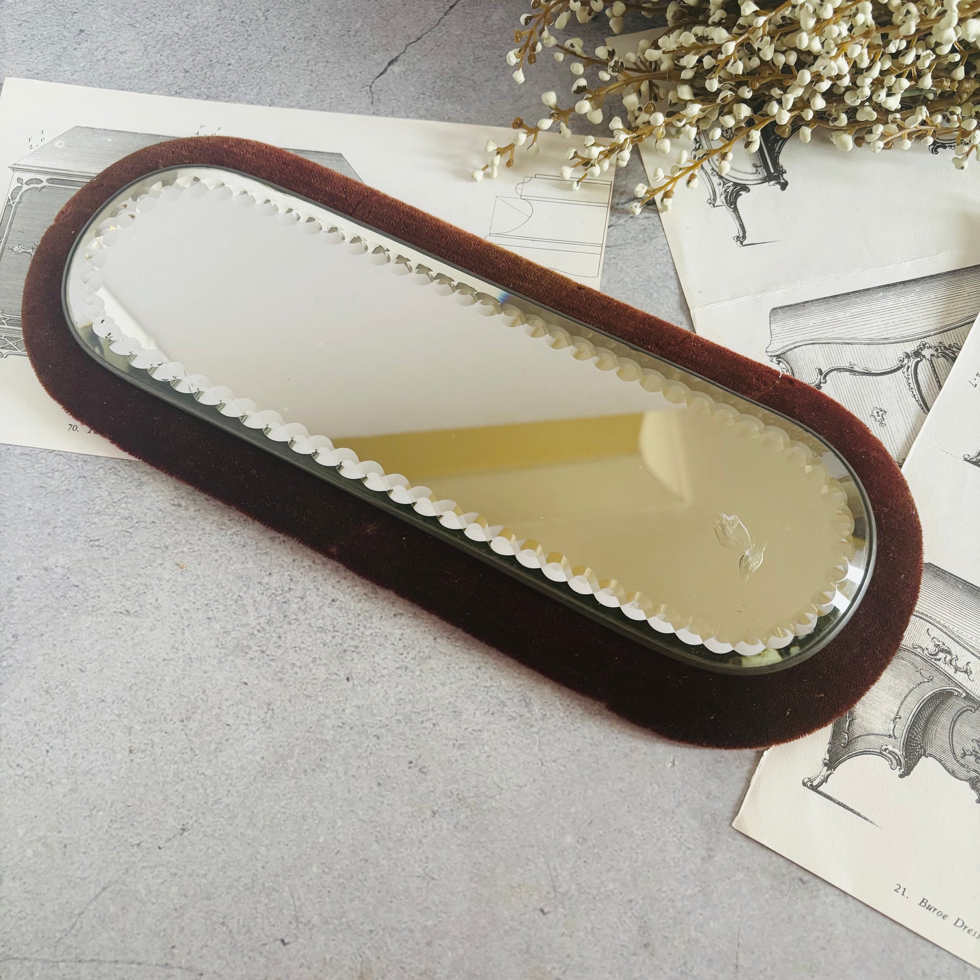Long oval mirror with brown frame on a textured surface with dried flowers.