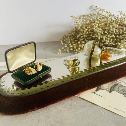 Gold jewelry set on a reflective surface with a vintage book and dried flowers in the background.