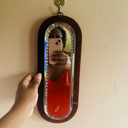 Person taking a mirror selfie with a decorative mirror on a beige wall.