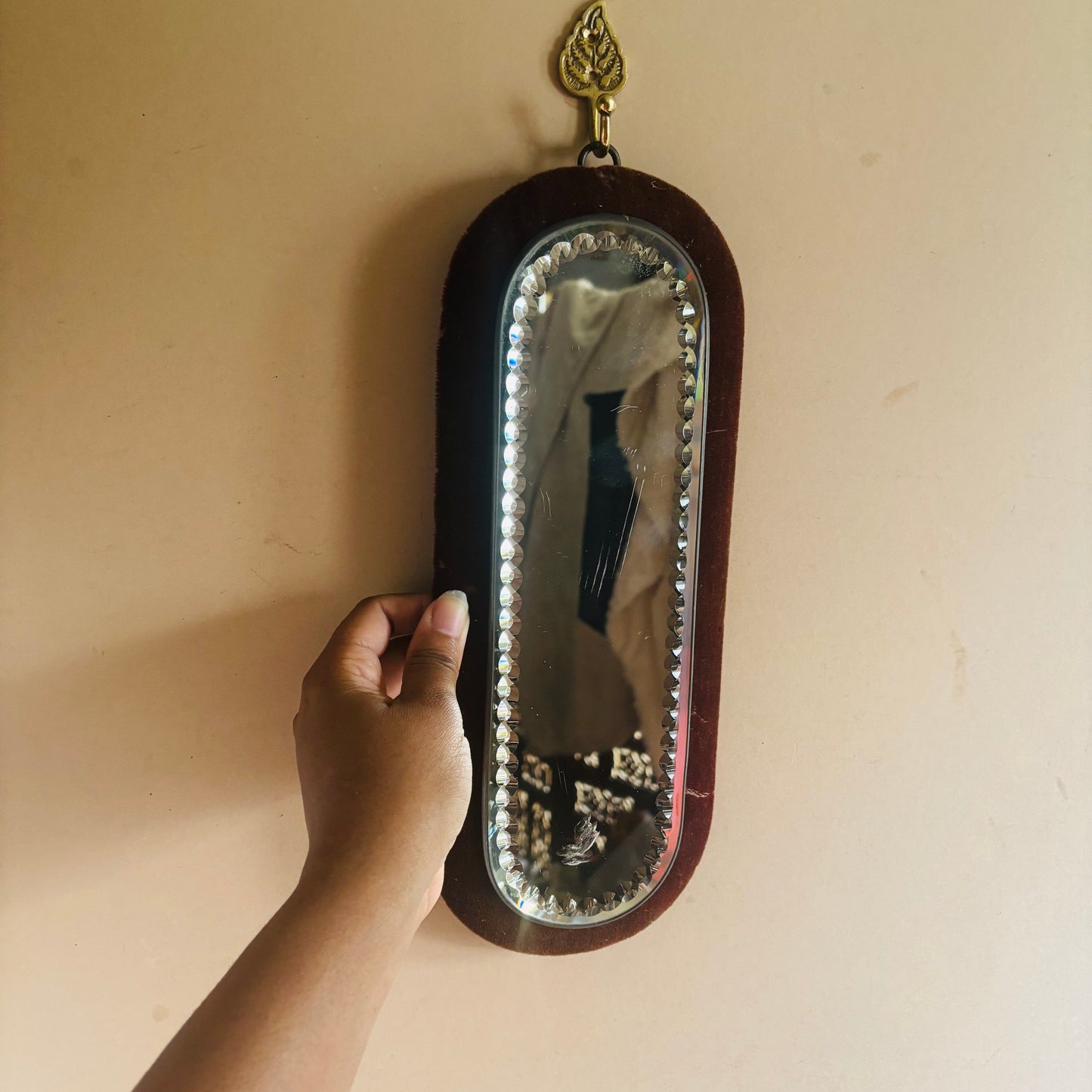 Hand holding a decorative mirror against a beige wall