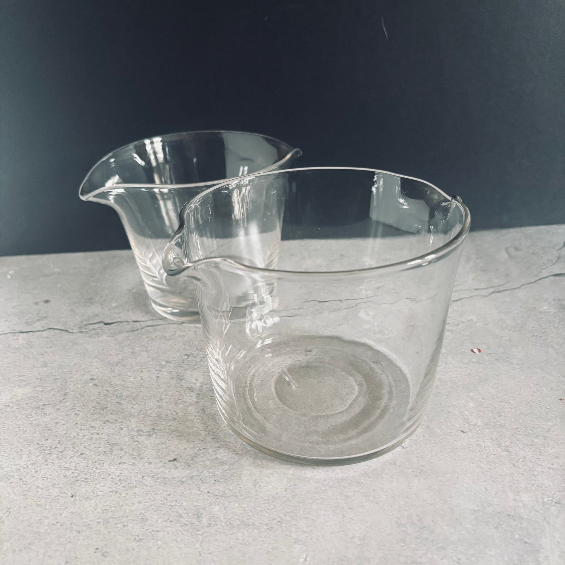 Two clear glass antique cooling rinsers on a textured gray surface with a dark background