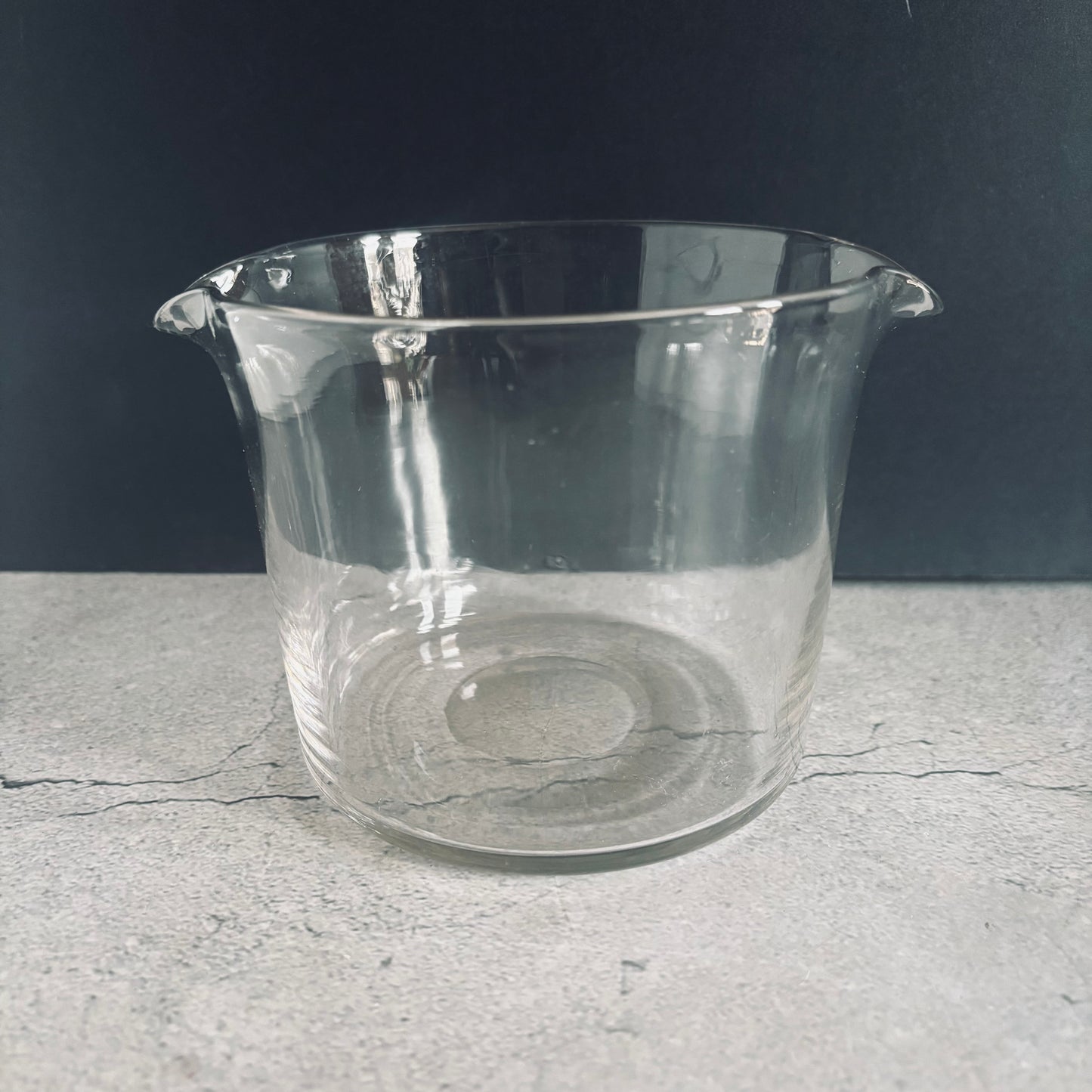 Clear glass beaker on a gray surface with a dark background