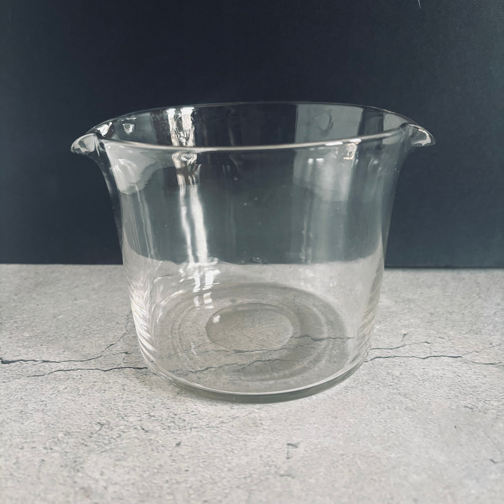 Clear glass beaker on a gray surface with a dark background