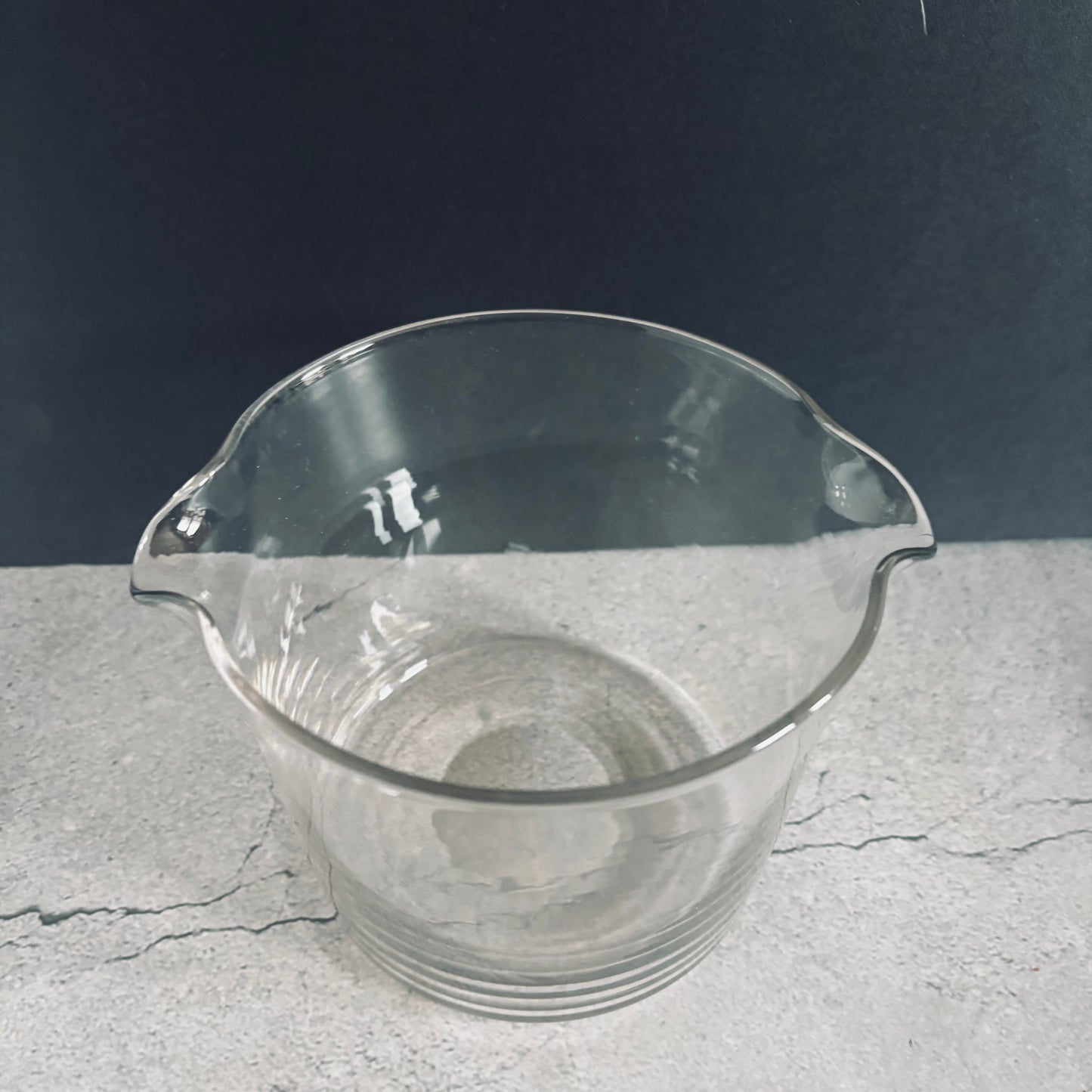 Clear glass beaker on a gray surface with a dark background